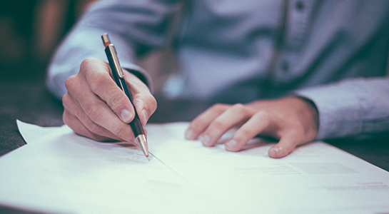 A man writing on a document with a pen.