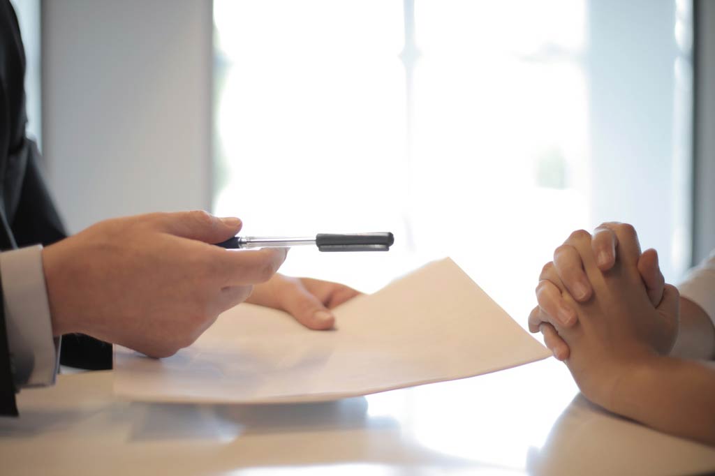 Hands on a desk extending paper and pen for registration.