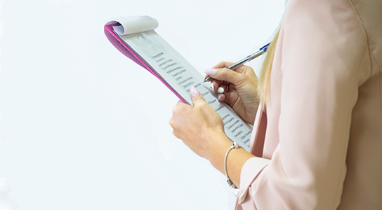 A woman notating on a document attached to a clipboard.